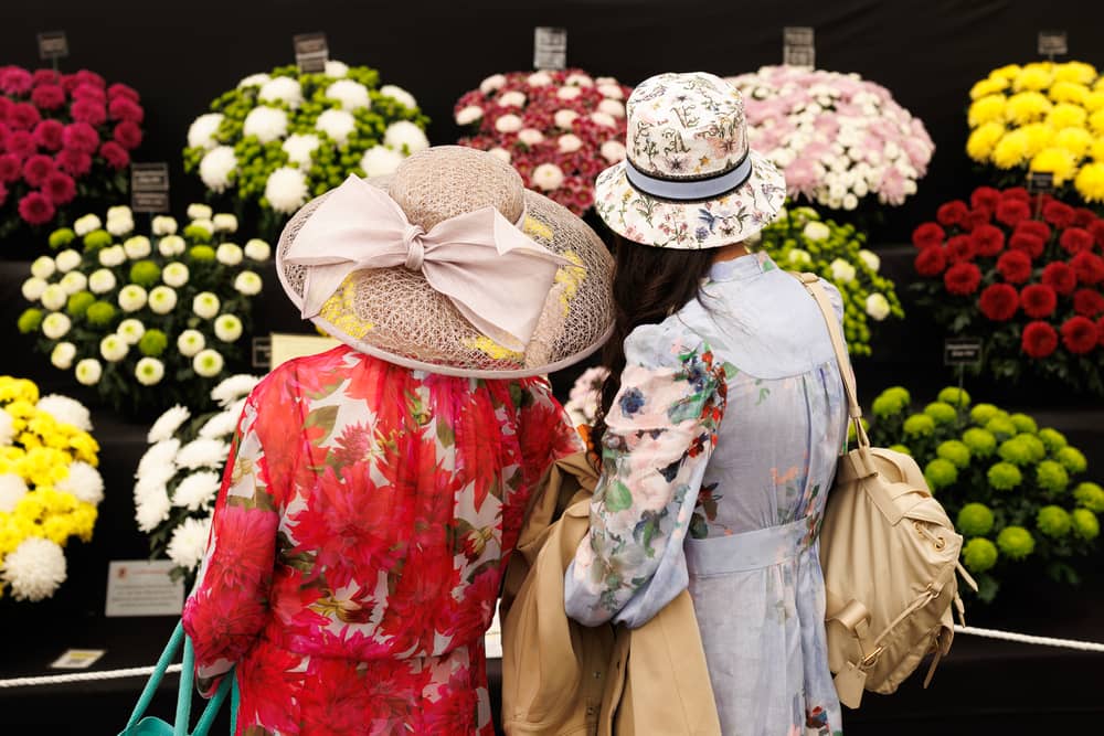Visitors wearing floral dresses and hats look at stands at RHS Chelsea Flower Show
