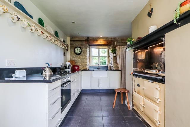 A traditional Aga and a modern cooker are within the kitchen with its end window and open stone wall feature.