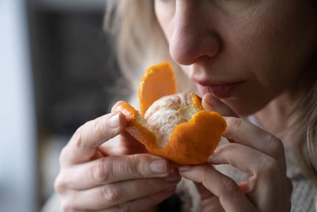 A woman trying to smell a fresh tangerine after losing sense of smell and taste due to Covid. Photo: Adobe