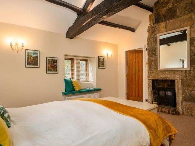 A beamed bedroom with carved stone and brick fireplace.