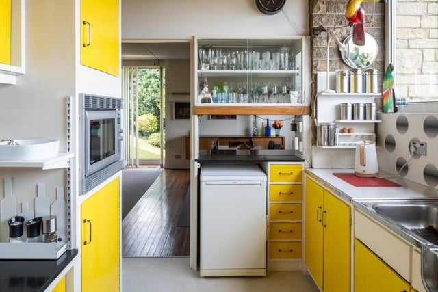 A colourful kitchen with yellow units topped by black Formica and stainless steel worktops.