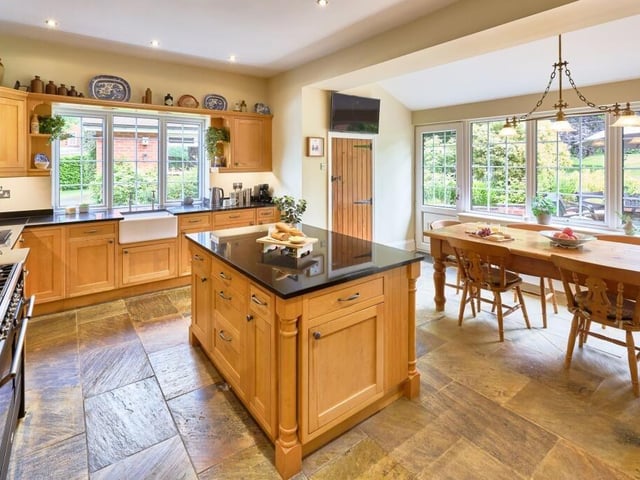The kitchen features shaker-style maple cabinets, black granite worktops and a central island set upon stone flooring.