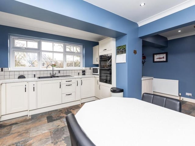 The kitchen has ivory shaker-style units with granite worktops, stone tile flooring and a built-in dining table.