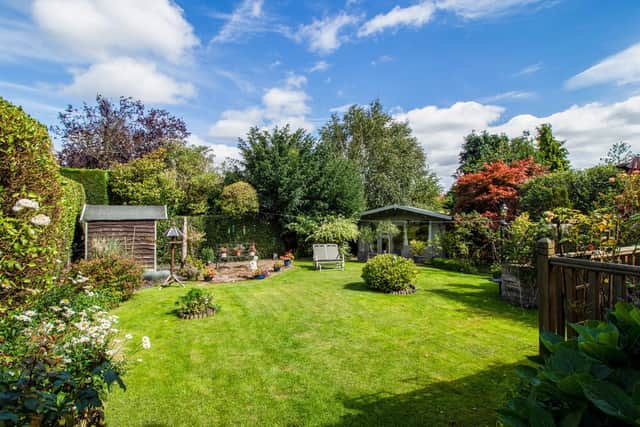 The private rear garden is lawned, with seating areas, a summer house, and surrounding trees, plants and shrubs.