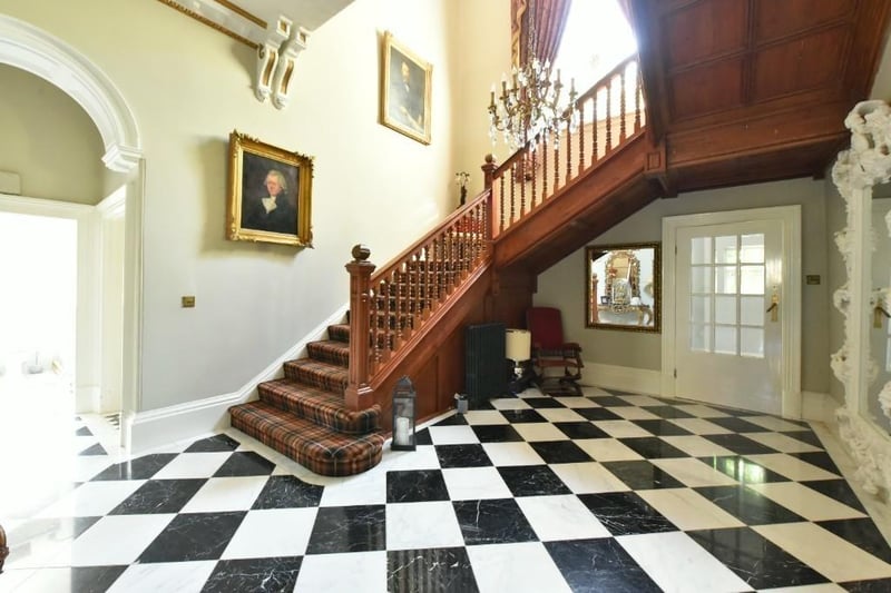 The vast staircase in the hallway has chessboard style flooring and ornate coving to ceiling