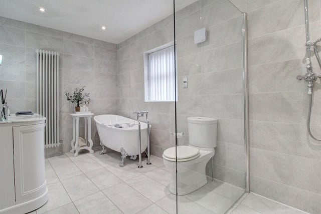 The modern four piece family bathroom is fully tiled from floor to ceiling and comprises and features a large walk in rainfall shower with glass screen and wet room drainage, a feature freestanding claw foot bath and a marble topped vanity unit.