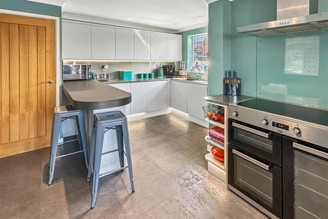 The kitchen features modern grey units to wall and floor plus a breakfast bar and two large windows allowing plenty of light in.