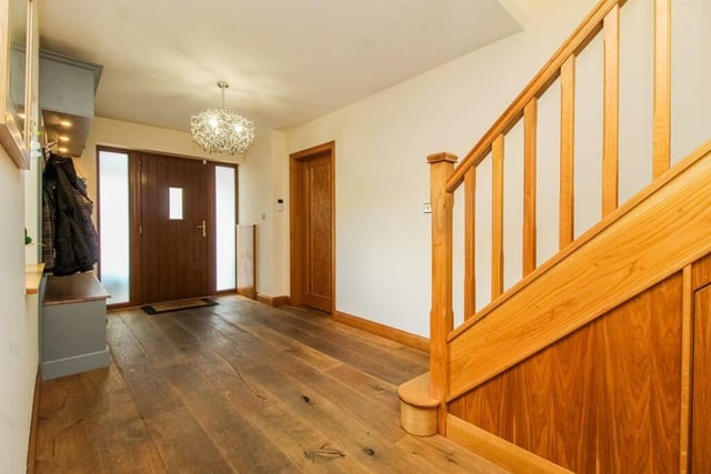 The entrance hall features a wide front entrance door with side screens, solid wood flooring, an additional window to the side and stairs to the first floor with understair cupboard.