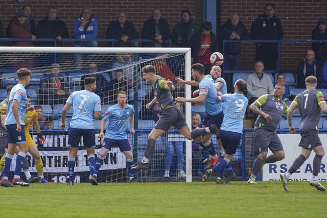 Ossett United players challenge for a high ball into the box.