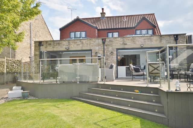 A large decked seating area with glass balustrade leads down to the lawn at the rear of the Monk Fryston property.