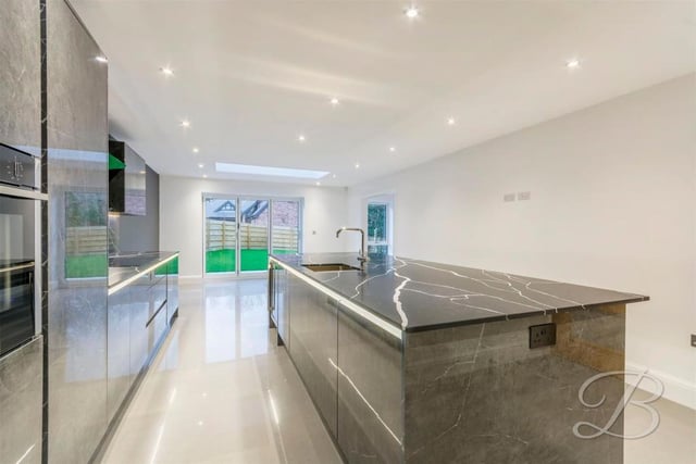 Another view of the high-quality, bespoke kitchen. It features luxurious, branded appliances and slick work-surfaces. At the far end, doors lead out on to the garden at the back.