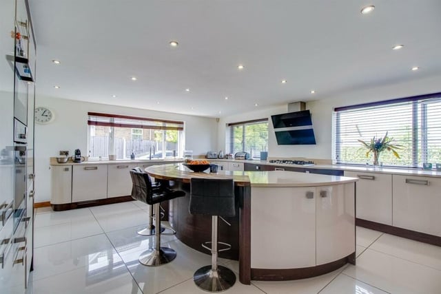 This lovely kitchen features underfloor heating, a range of high gloss handleless base units with extensive granite work surface over, an integrated stainless steel sink with a mixer tap and a curved island unit breakfast bar with base units.