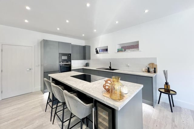 The open-plan living area seamlessly integrates with a sleek, modern kitchen, featuring a sleek sink, an integrated oven, a hob, and an elegant extractor hood suspended above.