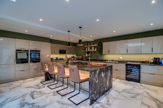 In the open plan dining area there is a lantern roof with shadow line lighting as well as a six door set of bi-folding doors. The marble flooring flows through into the adjoining kitchen area that is fitted with a broad range of contemporary style units with a stunning centrepiece matching island unit.