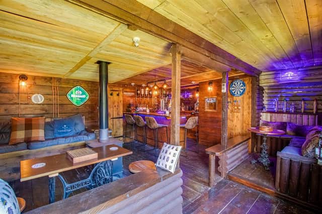 This converted log cabin has a fully operational bar, with a log burner, seating, and tables.