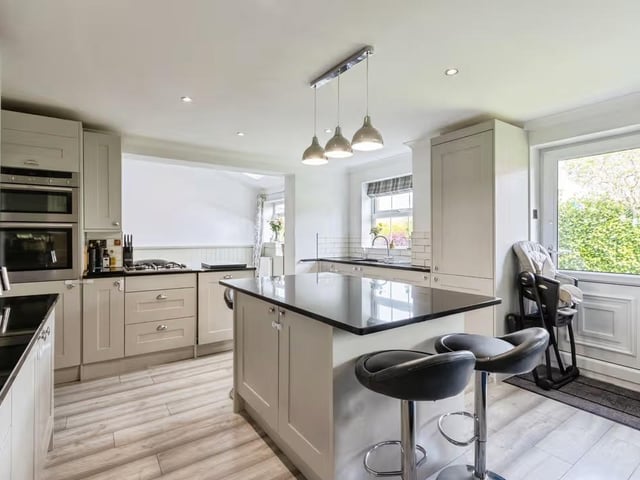 The contemporary kitchen features quartz worktops, a Belfast-style sink, integrated appliances and central island, while bi-fold and patio doors open directly onto the landscaped rear garden.
