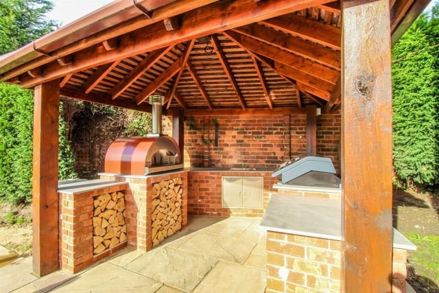To the side of the patio there is an outdoor kitchen under a rosemary tiled gazebo with a built in gas BBQ, fridge, sink and pizza oven.