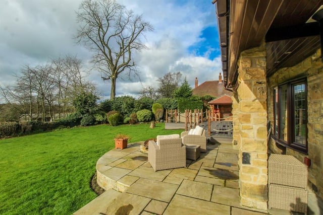 The lawned back garden extends from the patio seating areas and is bordered by an array of shrubs.