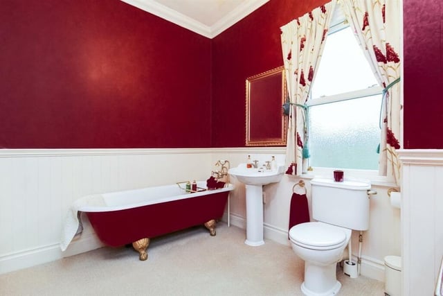 The bathroom includes decorative panelling, fitted storage, a low flush w.c., a pedestal wash basin and a roll top bath with a mixer tap and shower head attachment.