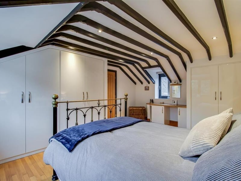 The principal bedroom features exposed wooden beams, bespoke fitted wardrobes and a dressing table area, alongside an en suite and a separate dressing room.