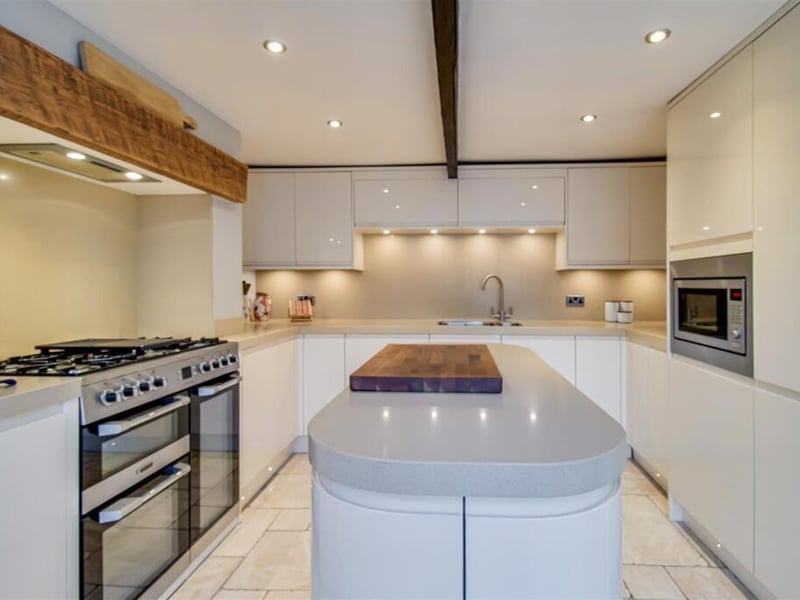 The kitchen includes a range of contemporary cream gloss soft close wall and base units, an integrated fridge/freezer, exposed wooden beams and an archway into the separate dining room.