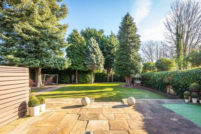 The walled rear garden has a flagstone patio with lawn and established trees, shrubs and plants.