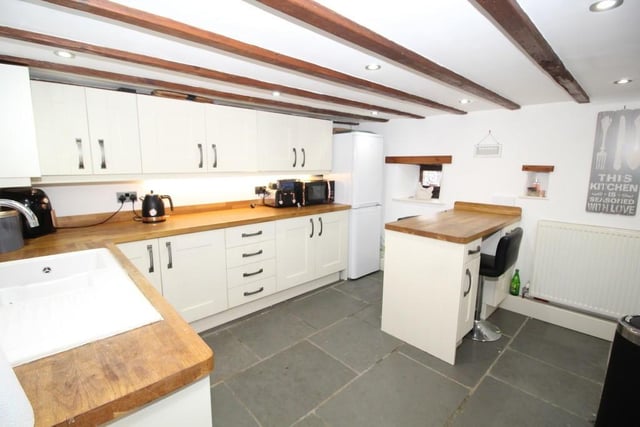 The beamed kitchen with shaker-style units and wooden worktops has a peninsula breakfast bar.