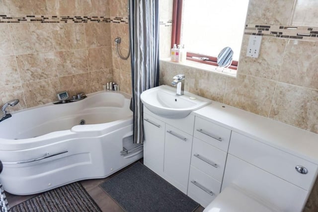A bathroom with a suite including a jacuzzi style bath and wash basin within vanity unit.