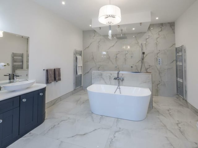 This impressive bathroom is characterised by porcelain wall and underfloor heating tiles, a free-standing bath, a glass shower wall with a rain head, and a full body shower.
