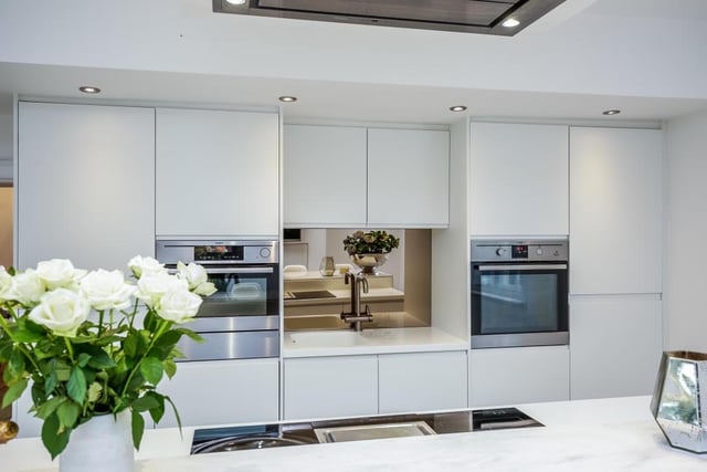The modern kitchen with French. doors out to a side terrace has fitted units with Corian worktops, integrated appliances, and a large central island with a raised breakfast bar, an induction hob, teppanyaki and wok.