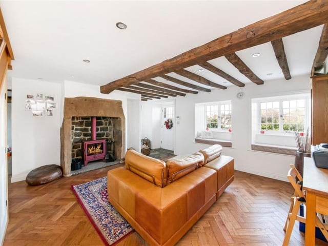 This sitting room with parquet flooring and window seats is made cosy by ceiling beams and Inglenook stone fireplace with a stove within.