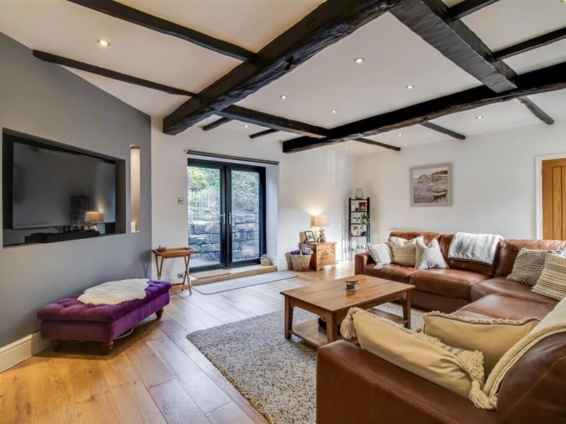This room features a glazed window to the front, exposed wooden beams, UPVC double glazed French doors to the rear, a feature media wall and a door to the further entrance hall.