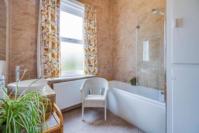 The tiled family bathroom has a washbasin vanity unit and bath with shower over.