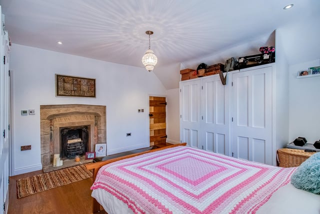 This bedroom has an original open cast iron fireplace with Yorkshire stone hearth and surround, a timber window and stone mullions to the side, inset ceiling spotlights, and built in wardrobes. Plug sockets have USB mounts and there is controlled lighting.