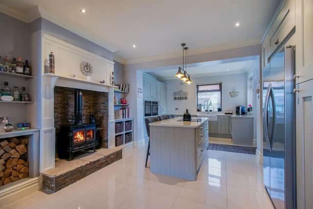 The kitchen, with shaker-style units, has a warming stove on a stone hearth.