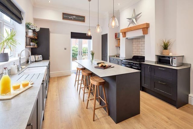 The kitchen features high ceilings and light walls contrasted with deep shaker-style units and grey worktops.